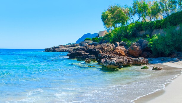A beach with clear blue water, sandy shore, and rocky outcrops with greenery. - Cas Ferrer Nou Hotelet (Alcúdia)