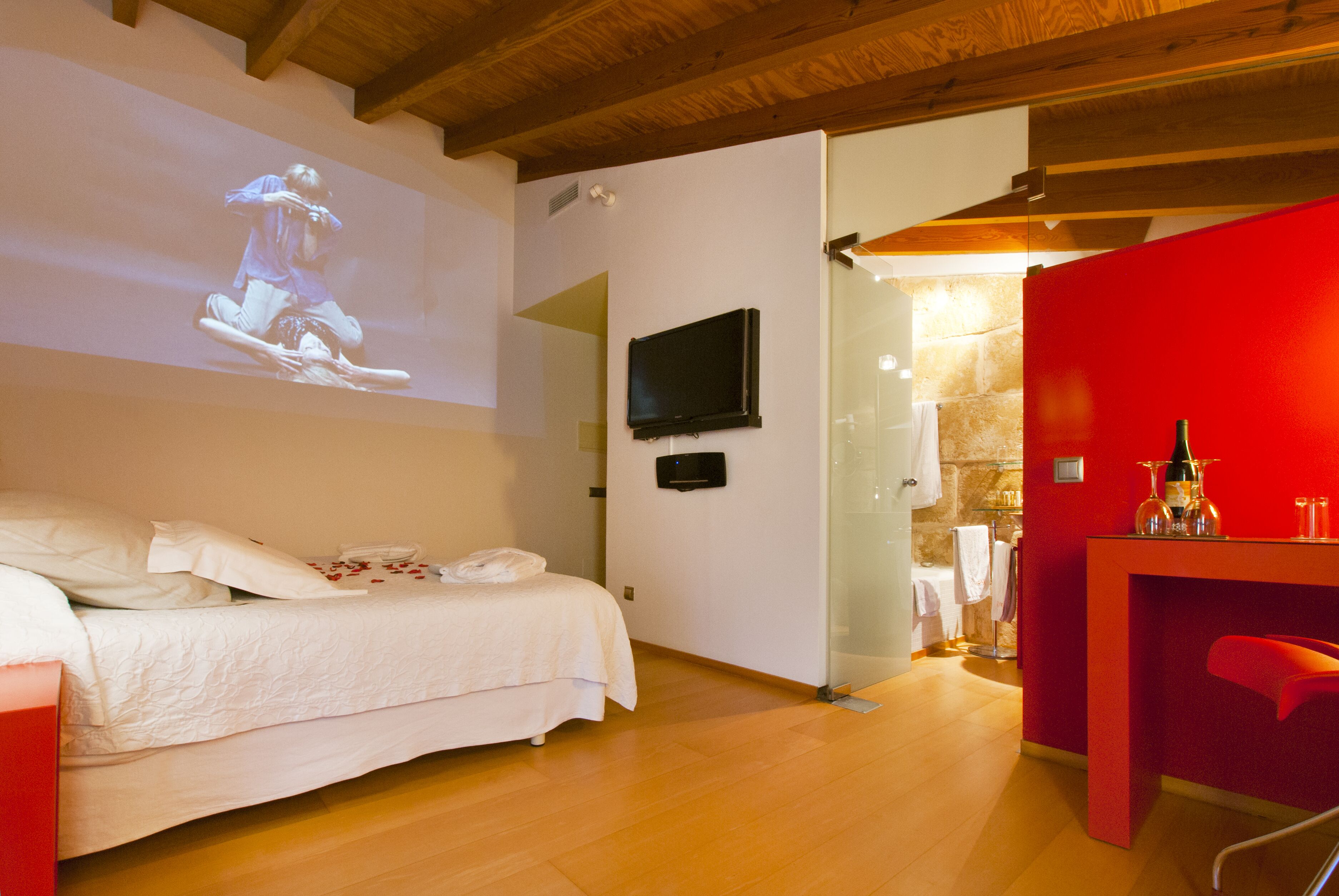 Ett hotellrum med en säng, en tv, en röd accentvägg och en duschhörna.