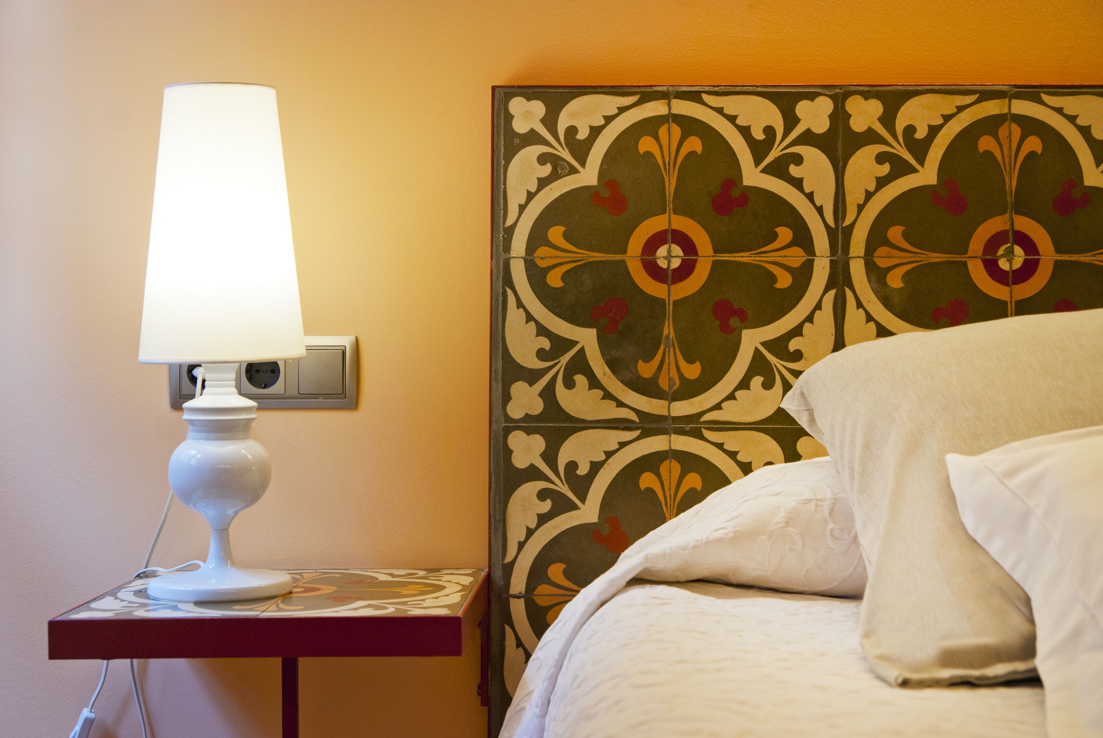 Cama com roupa de cama branca e mesa de cabeceira com abajur branco.