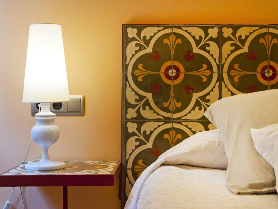 Cama com roupa de cama branca e mesa de cabeceira com abajur branco.
