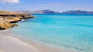 Una playa con aguas turquesas cristalinas, arena dorada y afloramientos rocosos.
