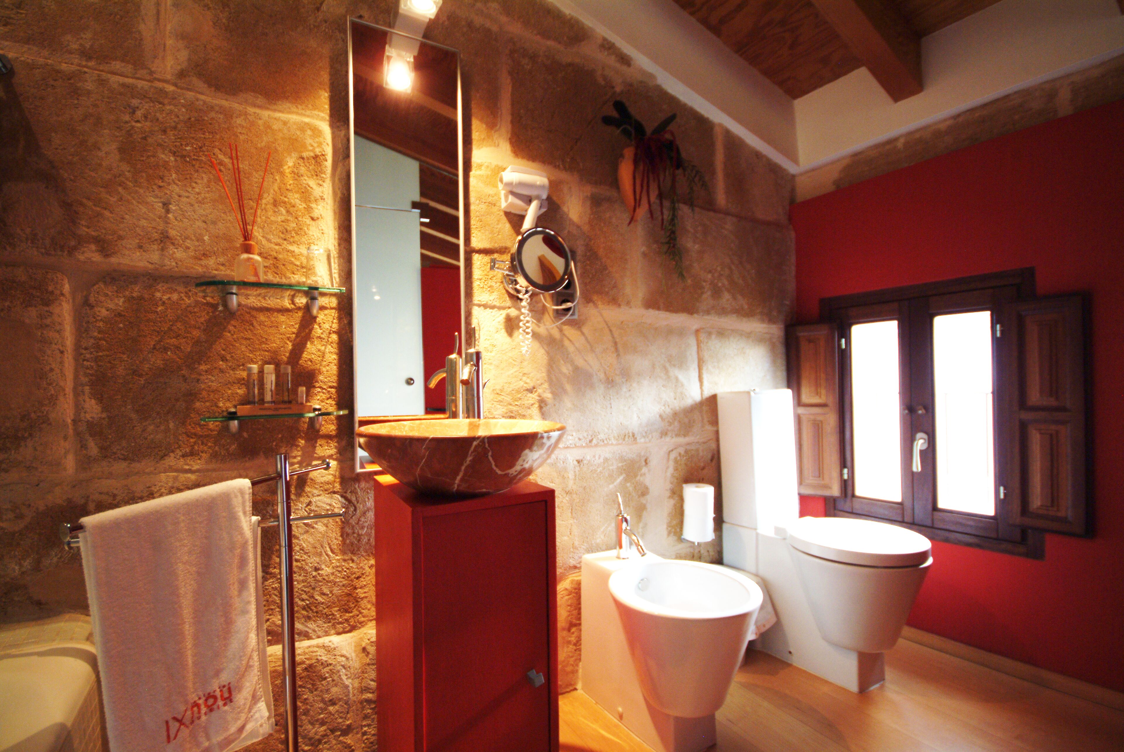 Un baño con pared de piedra, un mueble de madera, un lavamanos grande y un inodoro.