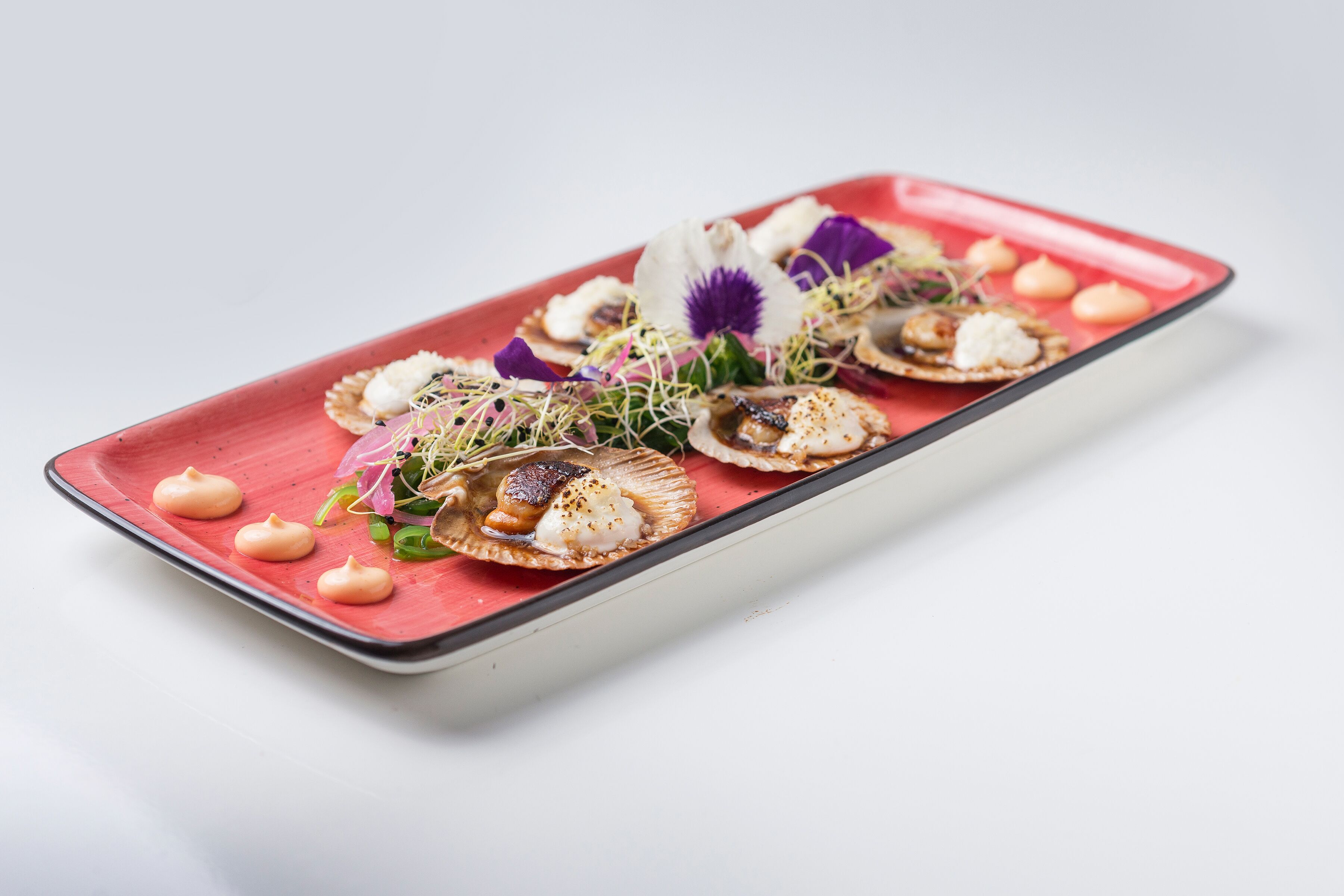 A rectangular plate with scallops, greens, and a purple flower on a white background.