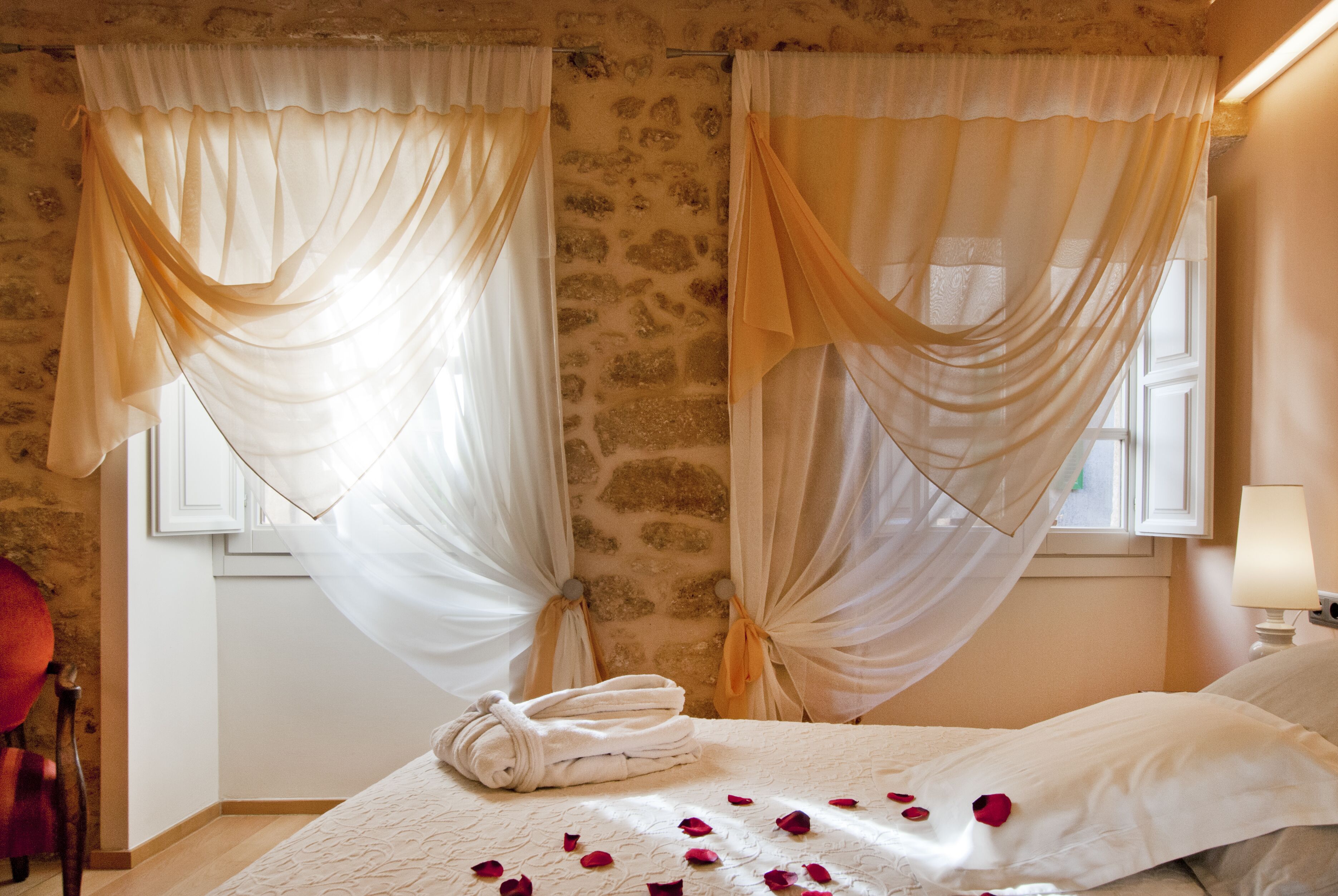 A room with a bed, draped curtains, a lamp, and a towel on the bed.