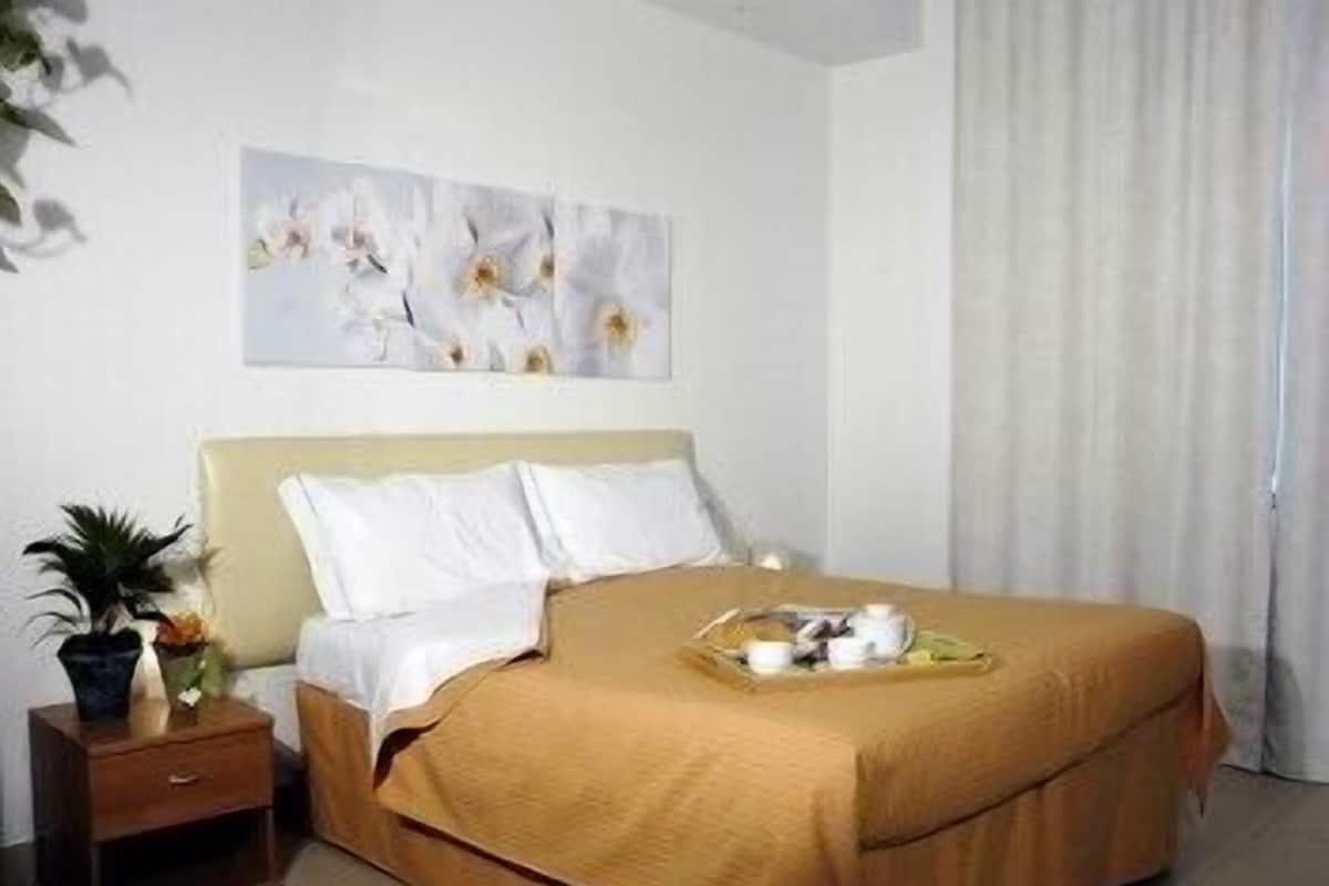 A hotel room with a bed, a nightstand, a potted plant, and a painting on the wall.