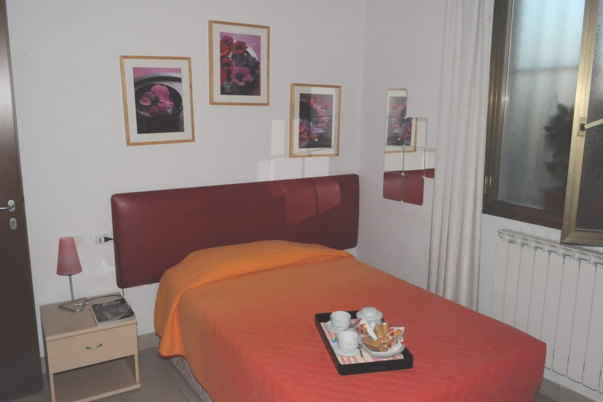 A hotel room with a red bedspread, a bedside table with a lamp, a tray with breakfast items, and framed pictures on the wall.