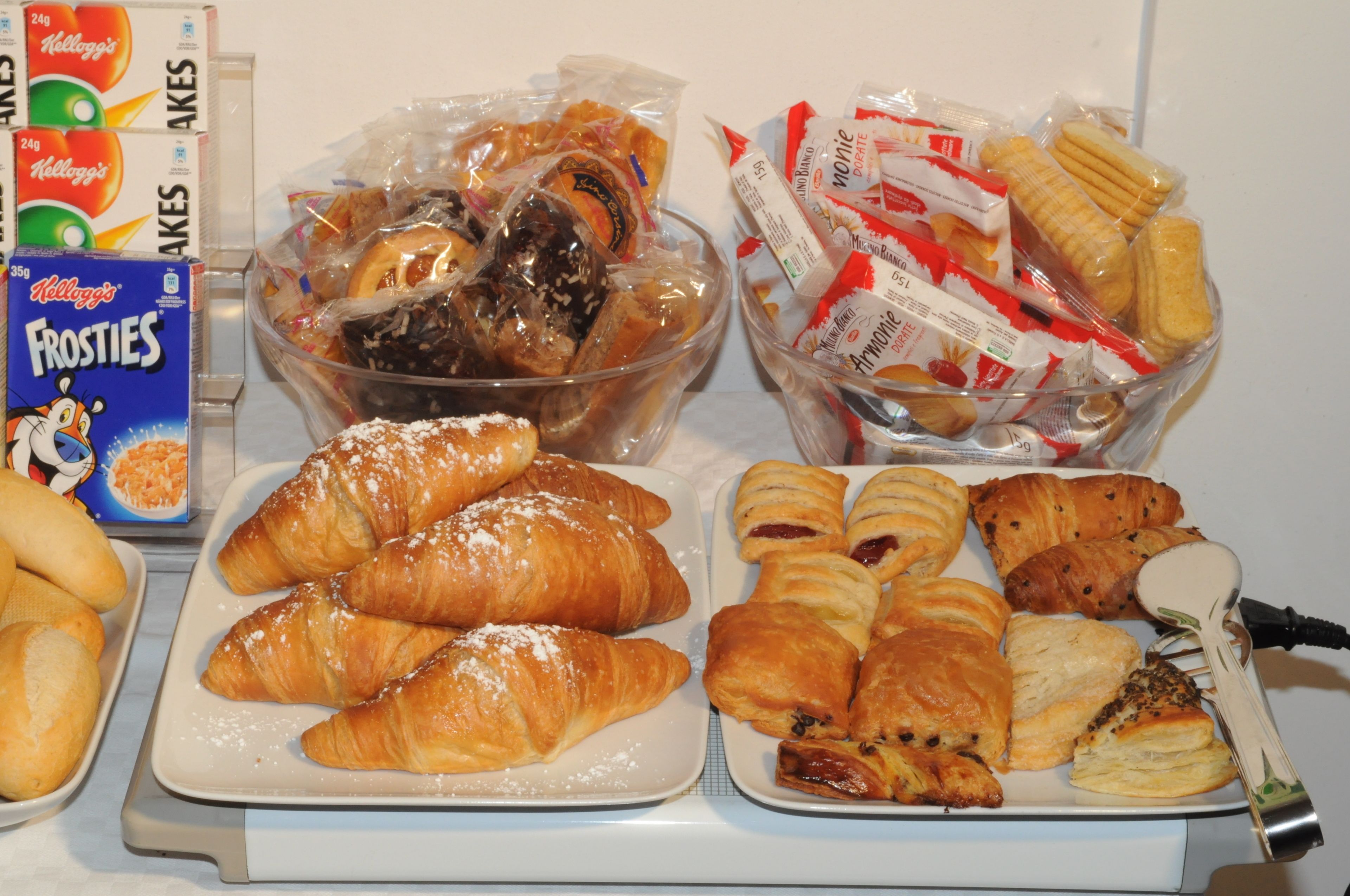 Un bufé de desayuno con diversas opciones de pastelería, incluyendo croissants y muffins, además de snacks como pretzels y barras de chocolate.