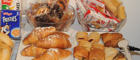 Un bufé de desayuno con diversas opciones de pastelería, incluyendo croissants y muffins, además de snacks como pretzels y barras de chocolate.
