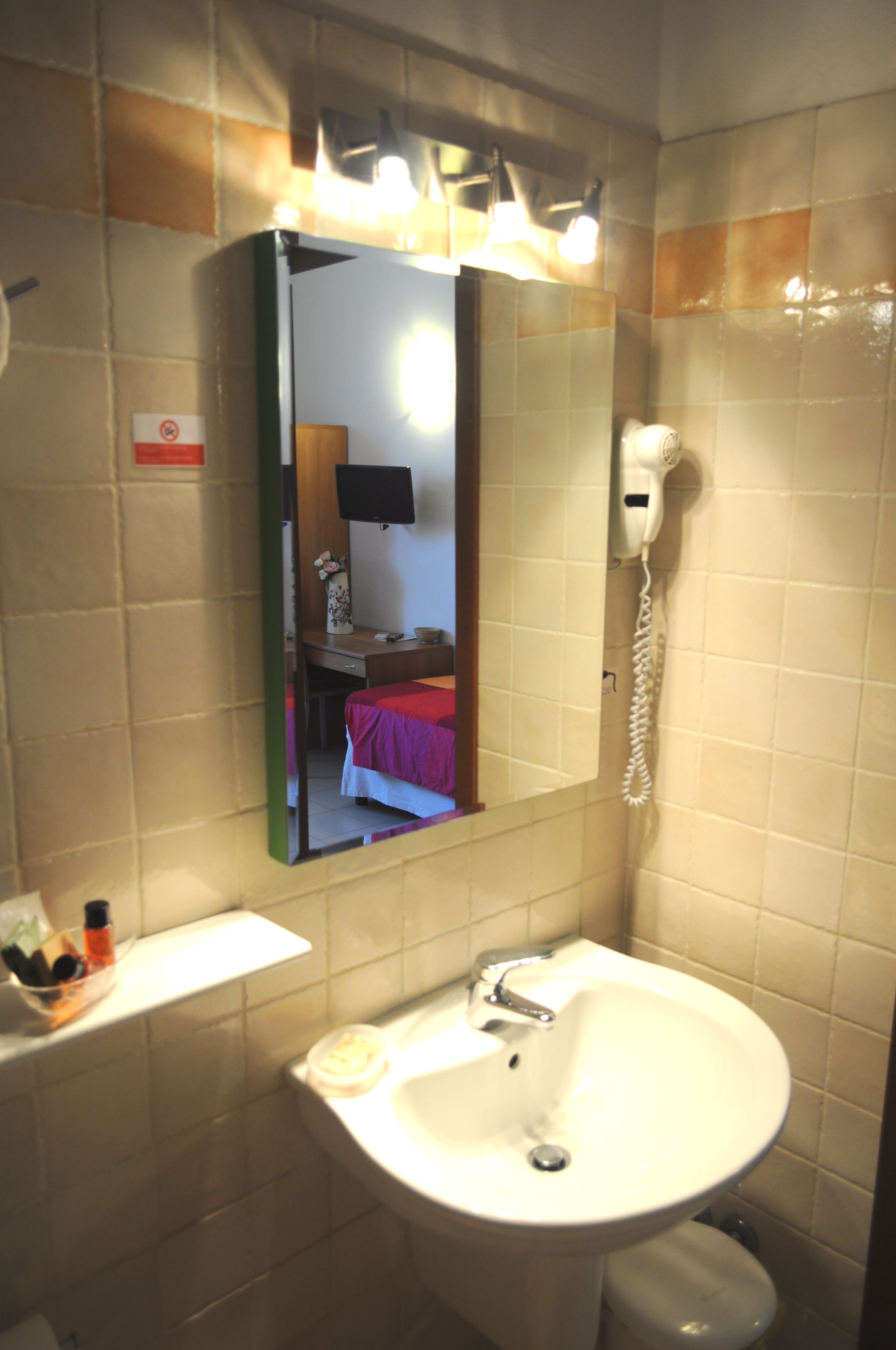 A bathroom with a sink, mirror, and a hairdryer on the wall.
