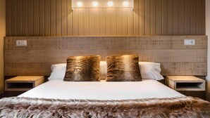 Habitación de hotel con cabecera de madera, dos mesitas de noche y una manta de piel en la cama.