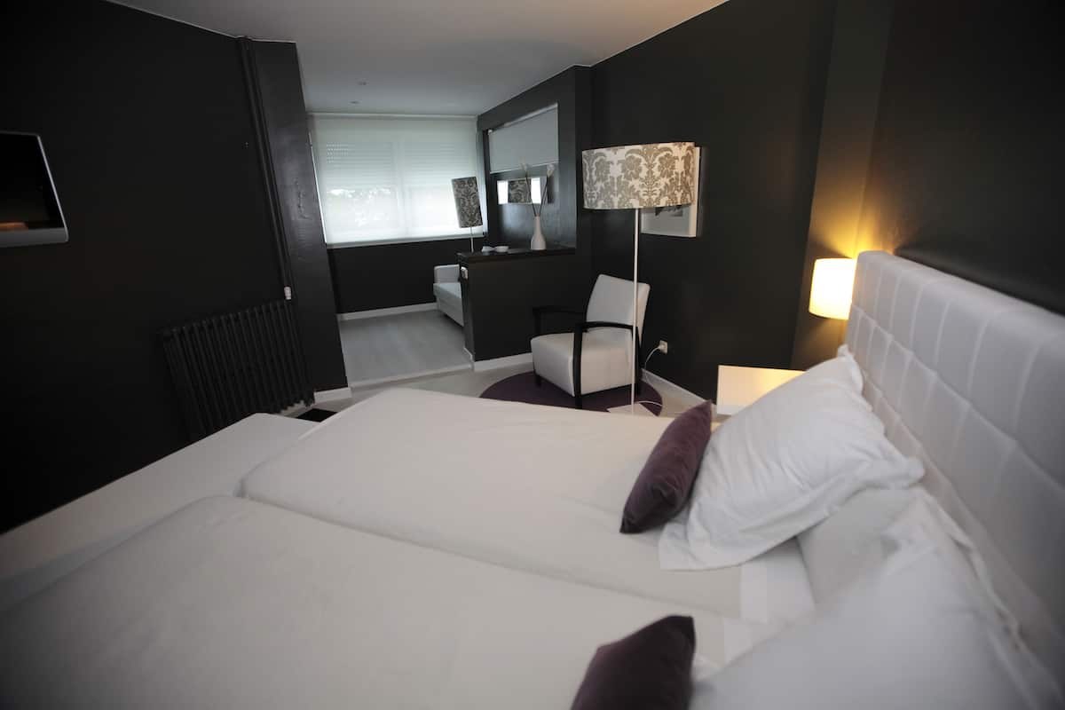 A hotel room with a large bed, a chair, a desk, and a lamp.