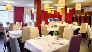Un restaurante con varias mesas, cada una con mantel blanco, sillas y copas de vino.