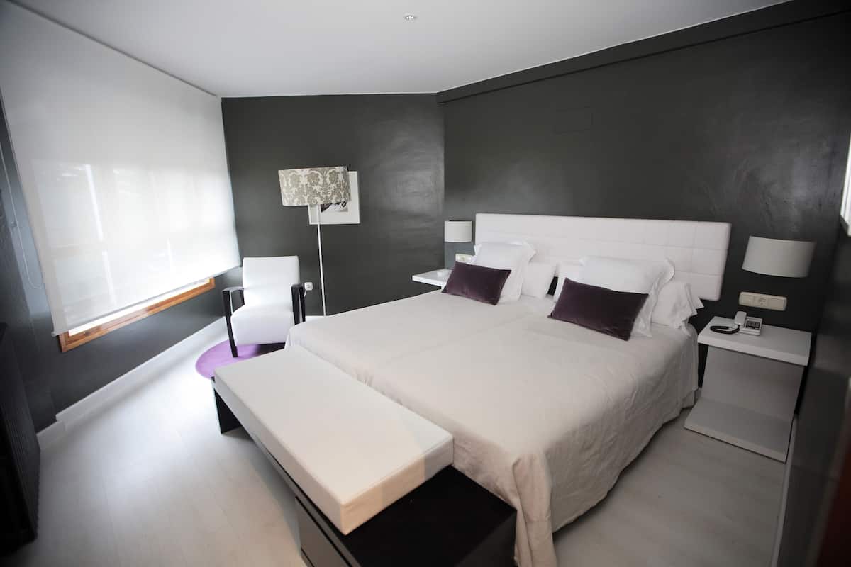 A modern bedroom with a large bed, bedside tables, a bench, and a floor lamp.