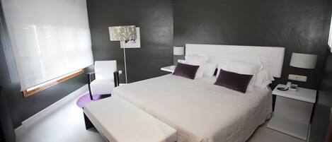 Un dormitorio moderno con una cama grande, mesitas de noche, un banco y una lámpara de pie.