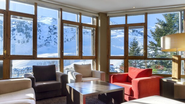 Una sala de estar moderna con ventanas amplias, una mesa de centro de madera y vistas a una montaña nevada.