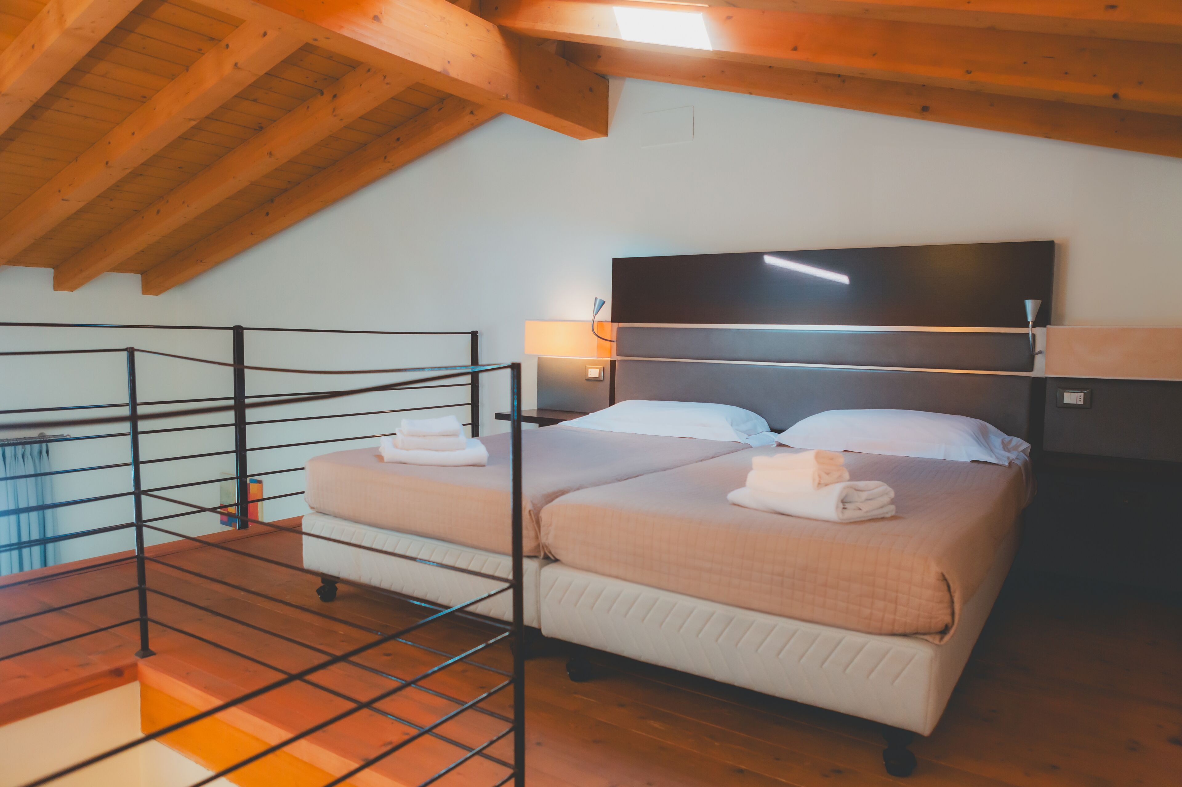 Ein Schlafzimmer mit zwei Betten, Holzbalkendecke, einem Fernseher und einem Balkon mit Metallgeländer.