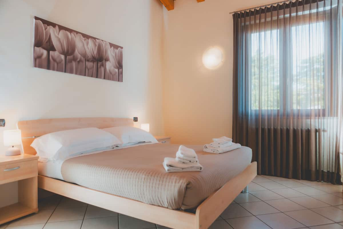 Una cama bien hecha con un cabecero, una mesita de noche con una lámpara y una ventana con cortinas.