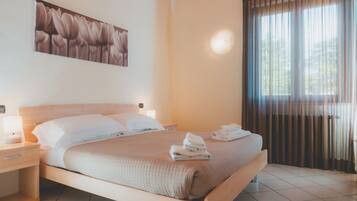 A neatly made bed with a headboard, a bedside table with a lamp, and a window with curtains.