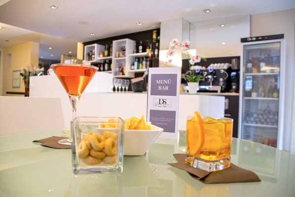 A bar area with a martini glass, a bowl of snacks, and a glass of amber-colored drink on a glass table.