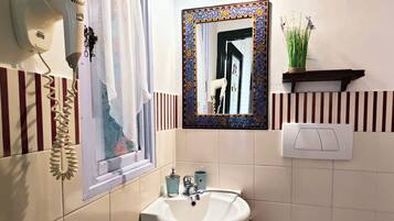 Een badkamer met een witte wastafel, een spiegel met decoratieve lijst, een haardroger, een toilet en een klein plankje met een plantje.