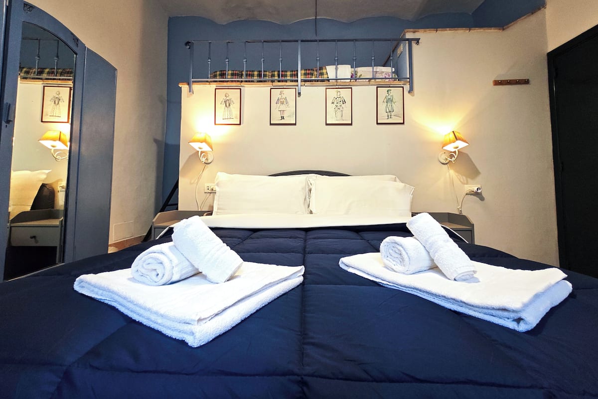 Quarto de hotel com uma cama grande, duas mesas de cabeceira, um espelho e quadros nas paredes.