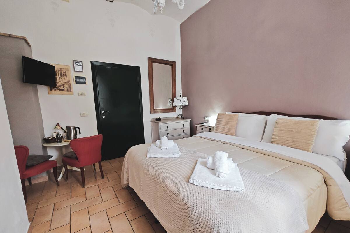 Quarto de hotel com cama, escrivaninha, cadeira, televisão e porta.