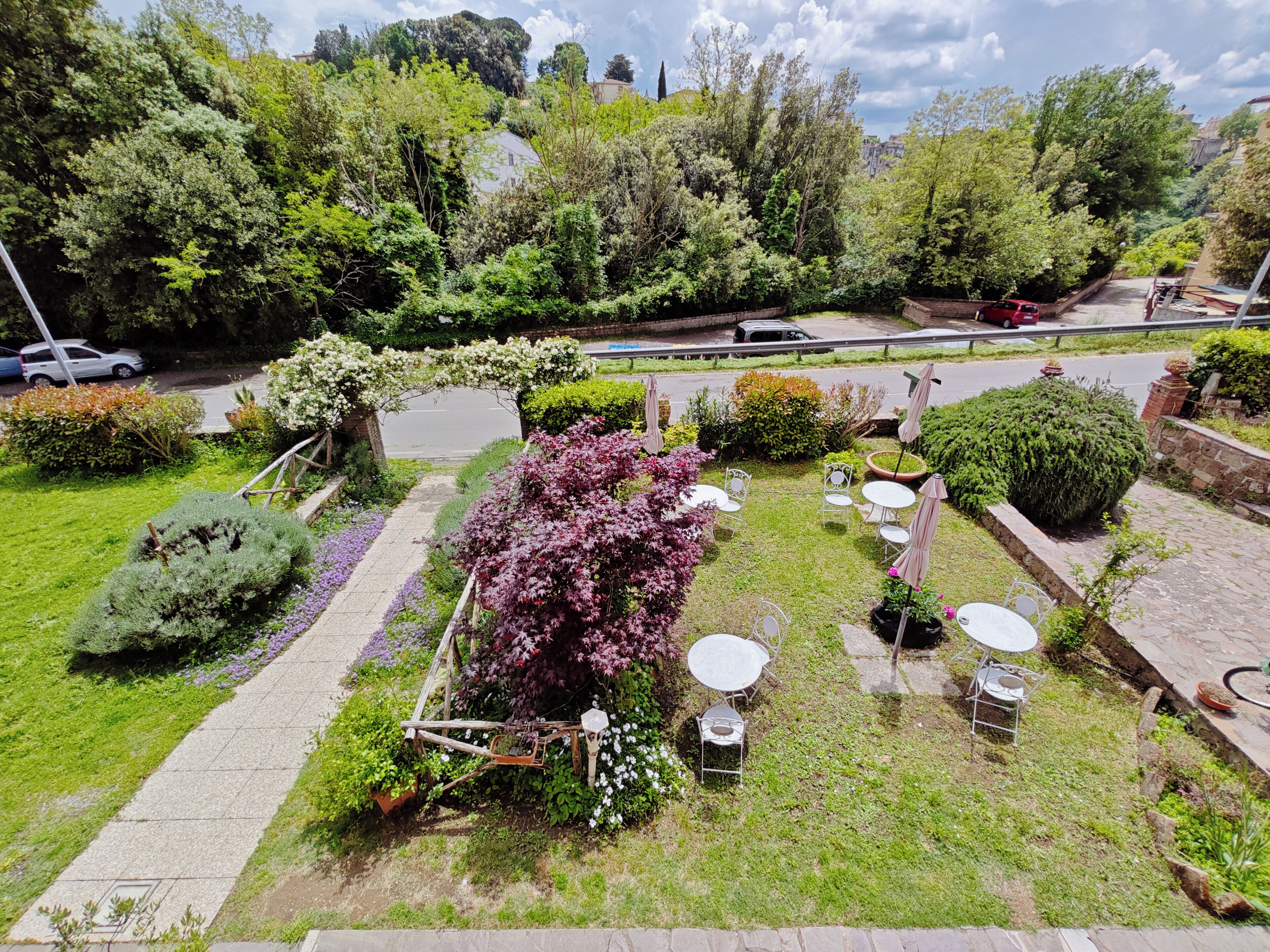 A garden with a paved walkway, seating area with tables and chairs, and various plants and shrubs.