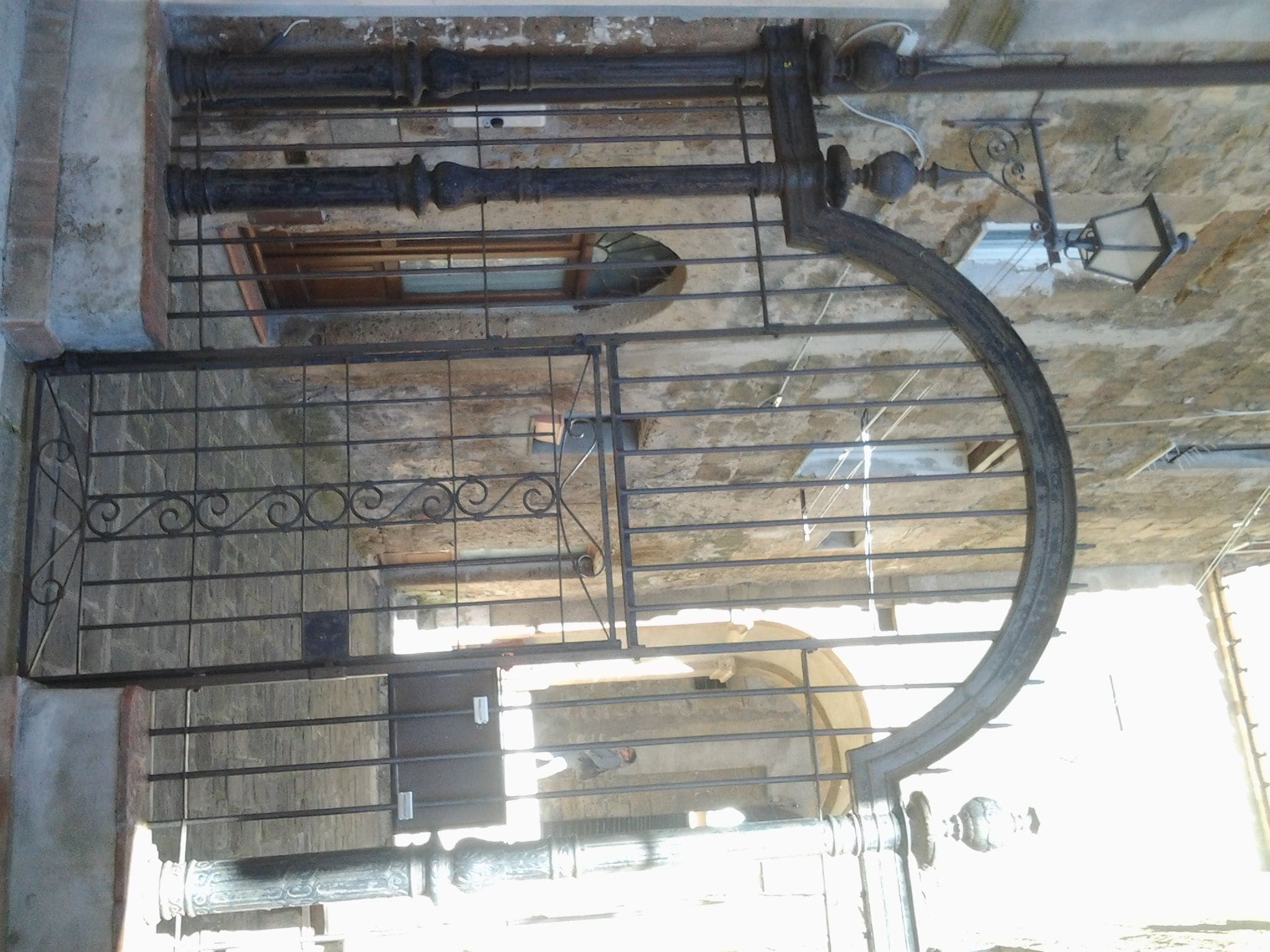 Een metalen hekwerk met een gebogen bovenkant, een decoratief patroon en een rechthoekige opening.