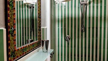 Ein Badezimmer mit einer Glasablage, einem weißen Waschbecken, einem Spiegel und einer Dusche mit grün-weiß gestreiften Fliesen.