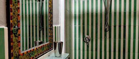Une salle de bain avec une étagère en verre, un lavabo blanc, un miroir et une douche dont les carreaux sont à rayures vertes.