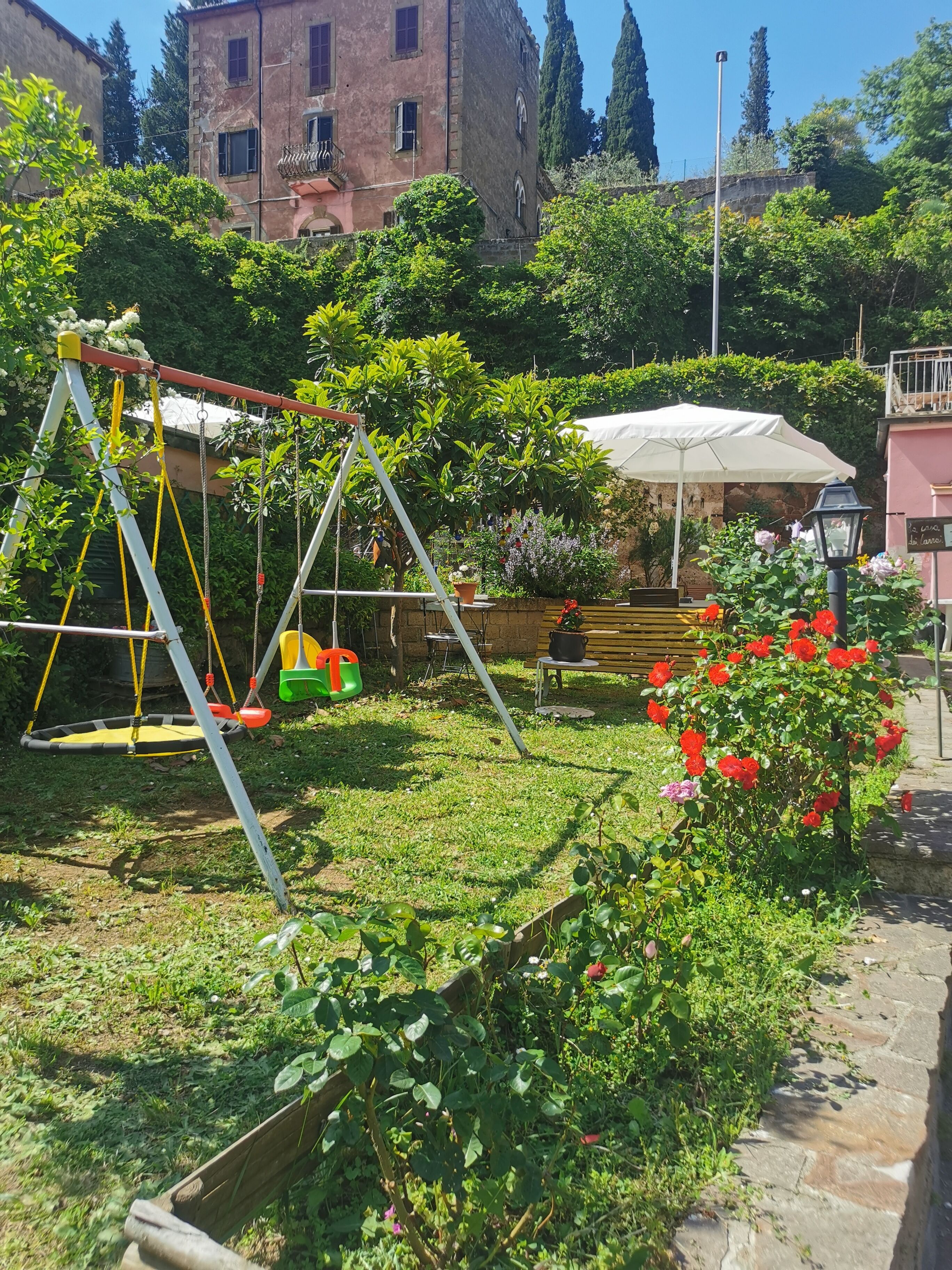 Un jardín con un columpio, una banca y una sombrilla blanca.