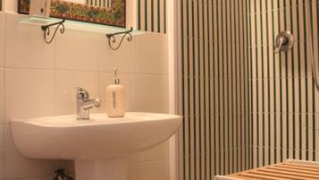 A bathroom with a sink, mirror, shower, and a shelf with toiletries.