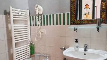 A bathroom with a white sink, a mirror with a decorative frame, a towel rack, a hairdryer, and a small round table with a basket.