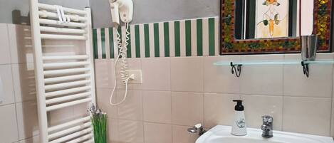 Un baño con un lavabo blanco, un espejo con un marco decorativo, un perchero para toallas, un secador de pelo y una mesita redonda con una cesta.