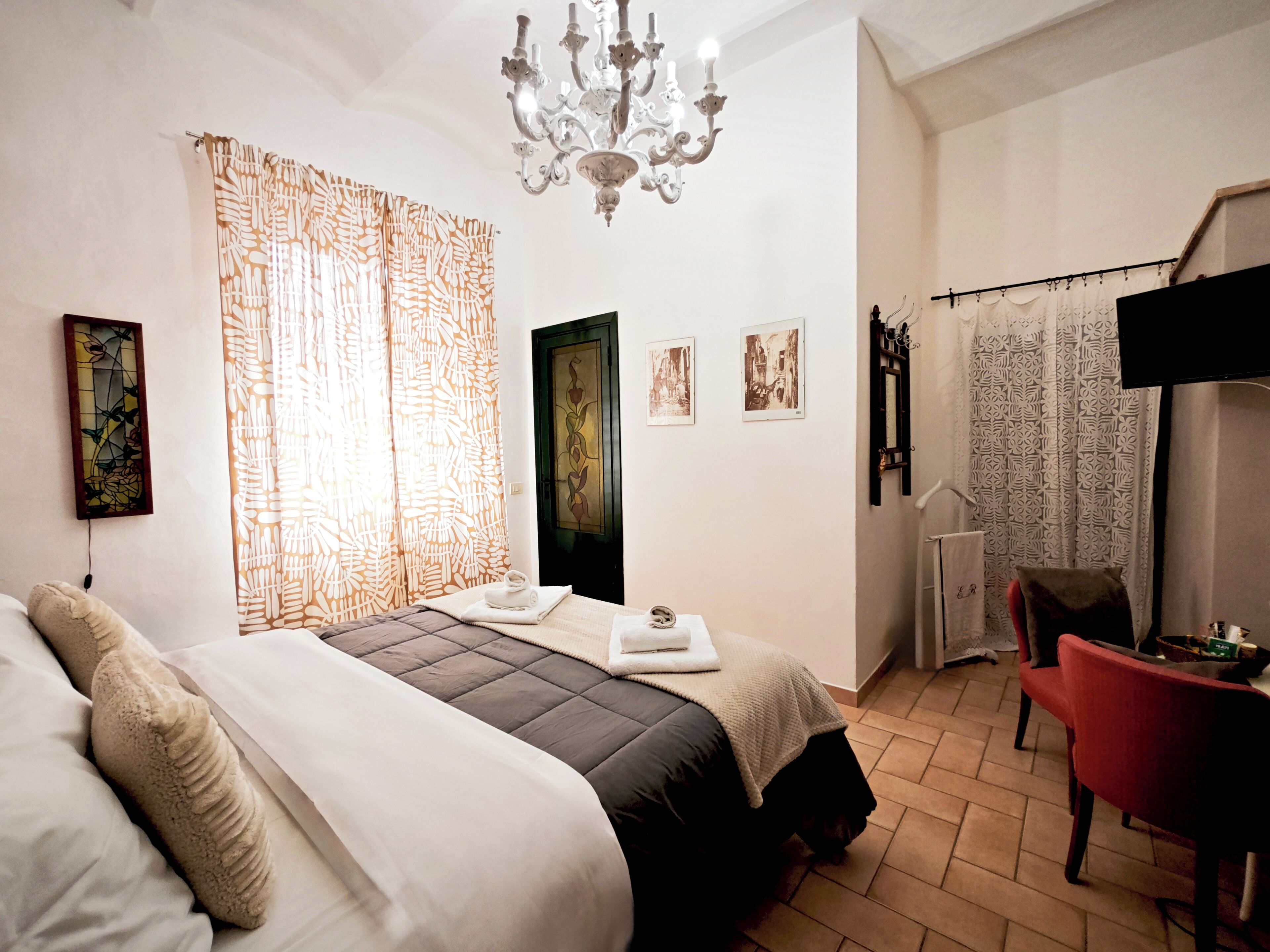 Habitación de hotel con cama, escritorio, silla, candelabro, cortinas y decoración en la pared.
