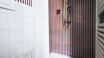 Un baño con inodoro blanco, ducha con pared a rayas rojas y blancas, y bañera blanca.