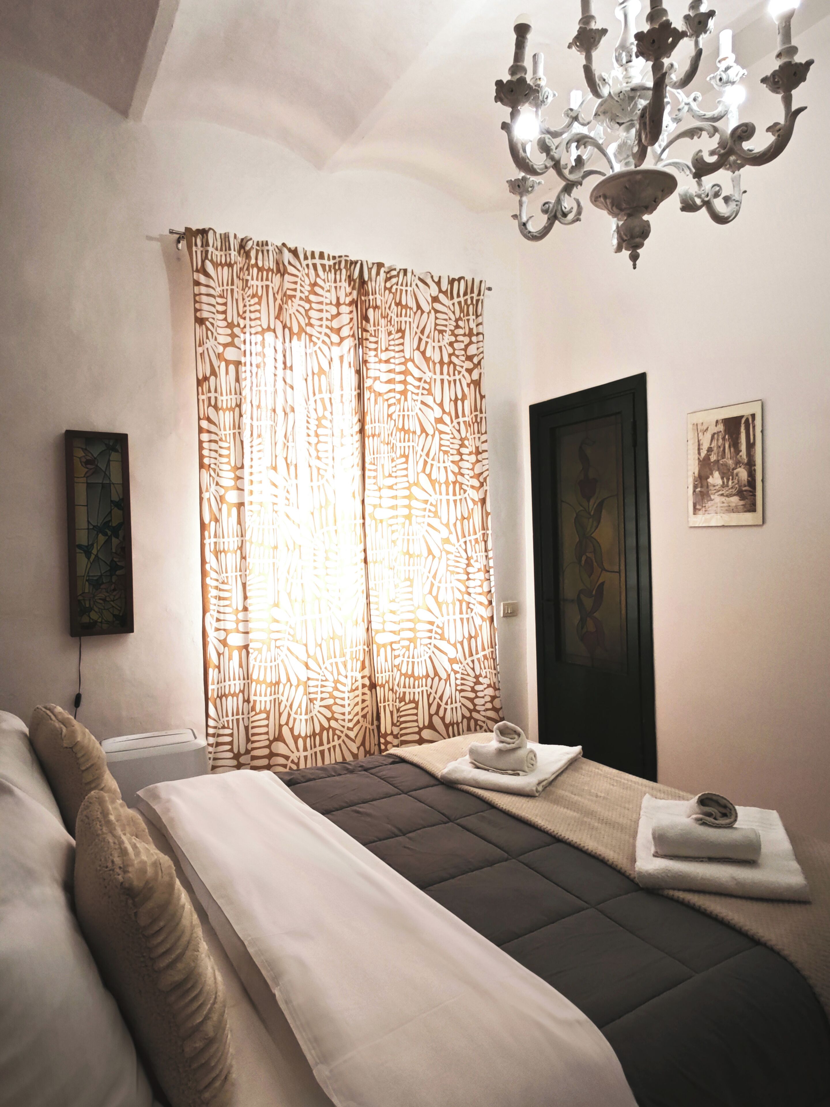 Un dormitorio con cama, lámpara de araña, puerta y cortina.
