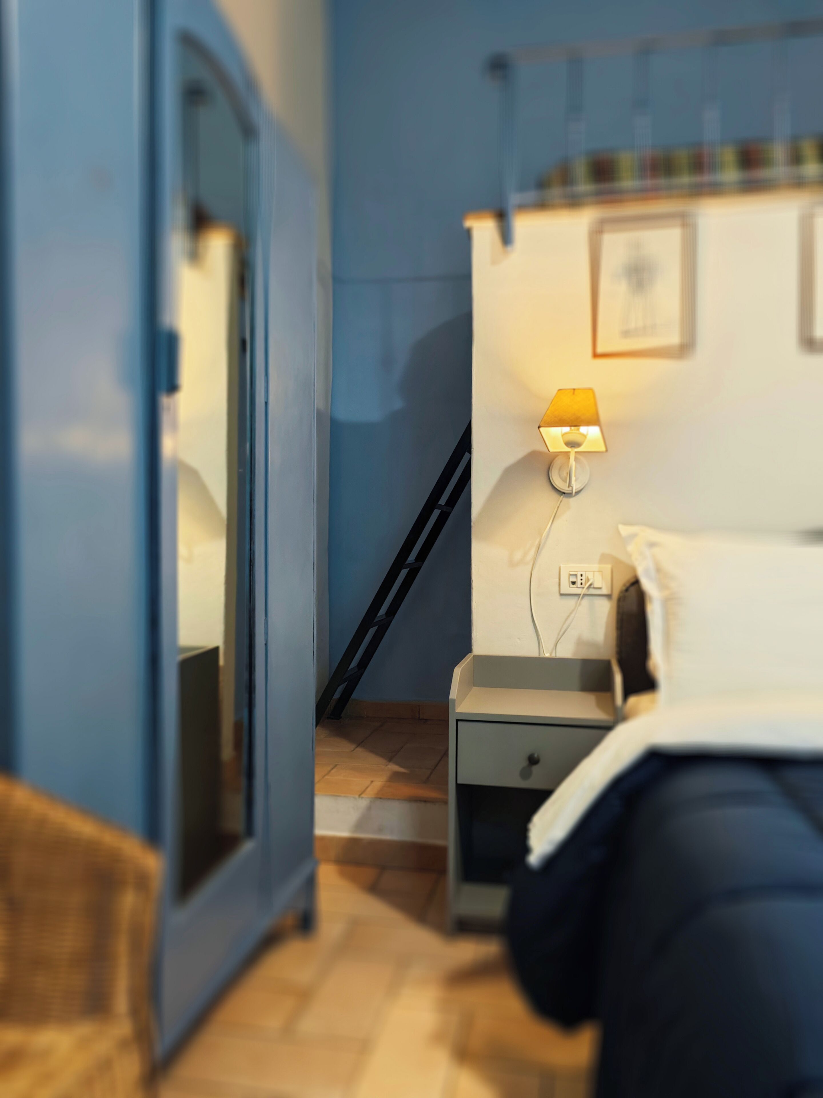 A bedroom with a bed, bedside table, lamp, and a ladder against the wall.