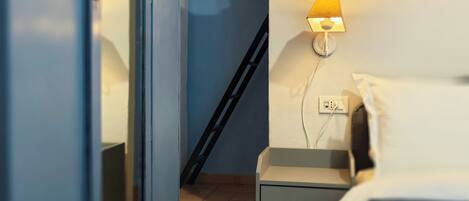 A bedroom with a bed, bedside table, lamp, and a ladder against the wall.