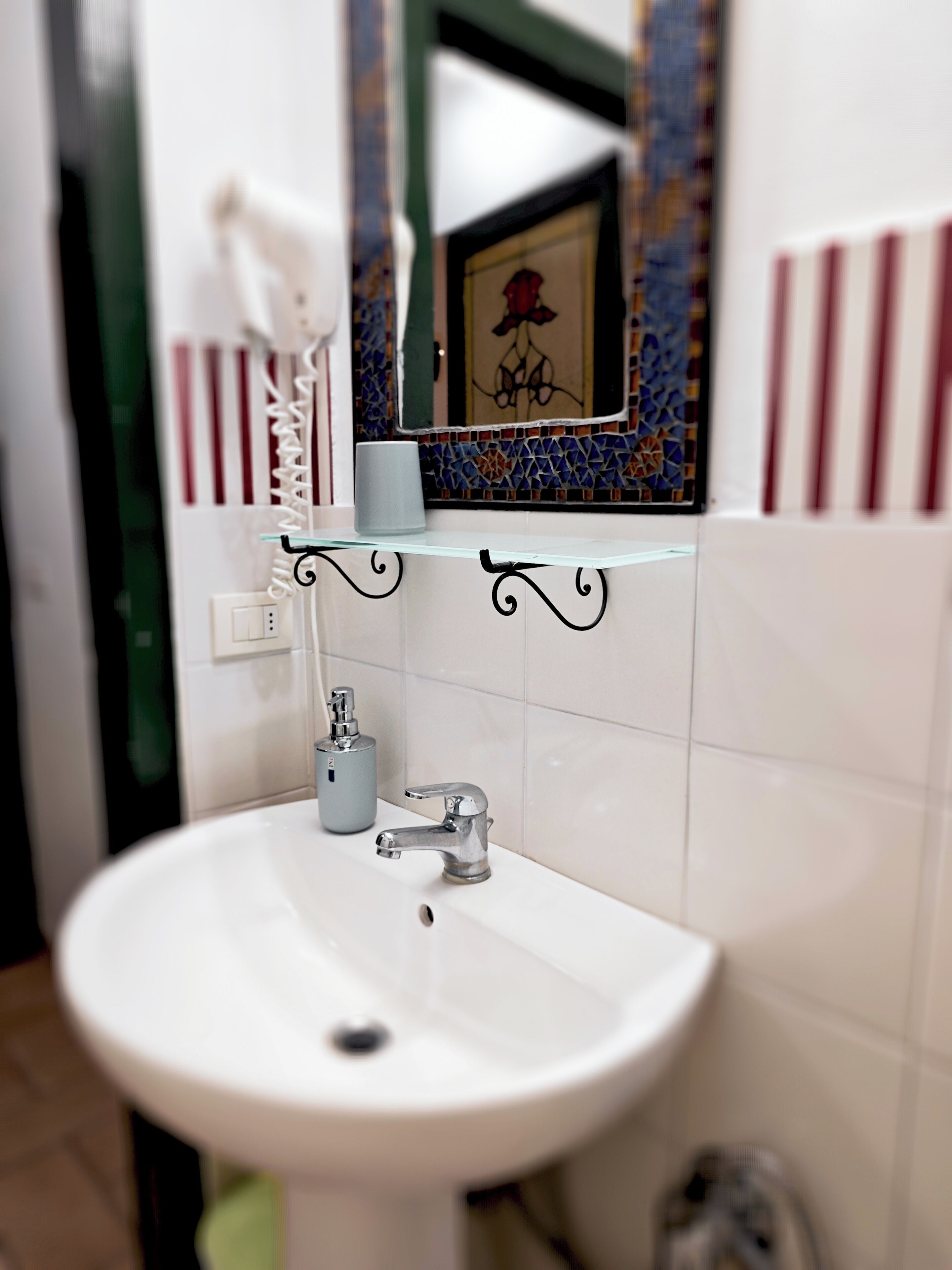 Un baño con un lavamanos blanco, una repisa de vidrio, un cuadro enmarco y una pared con azulejos.