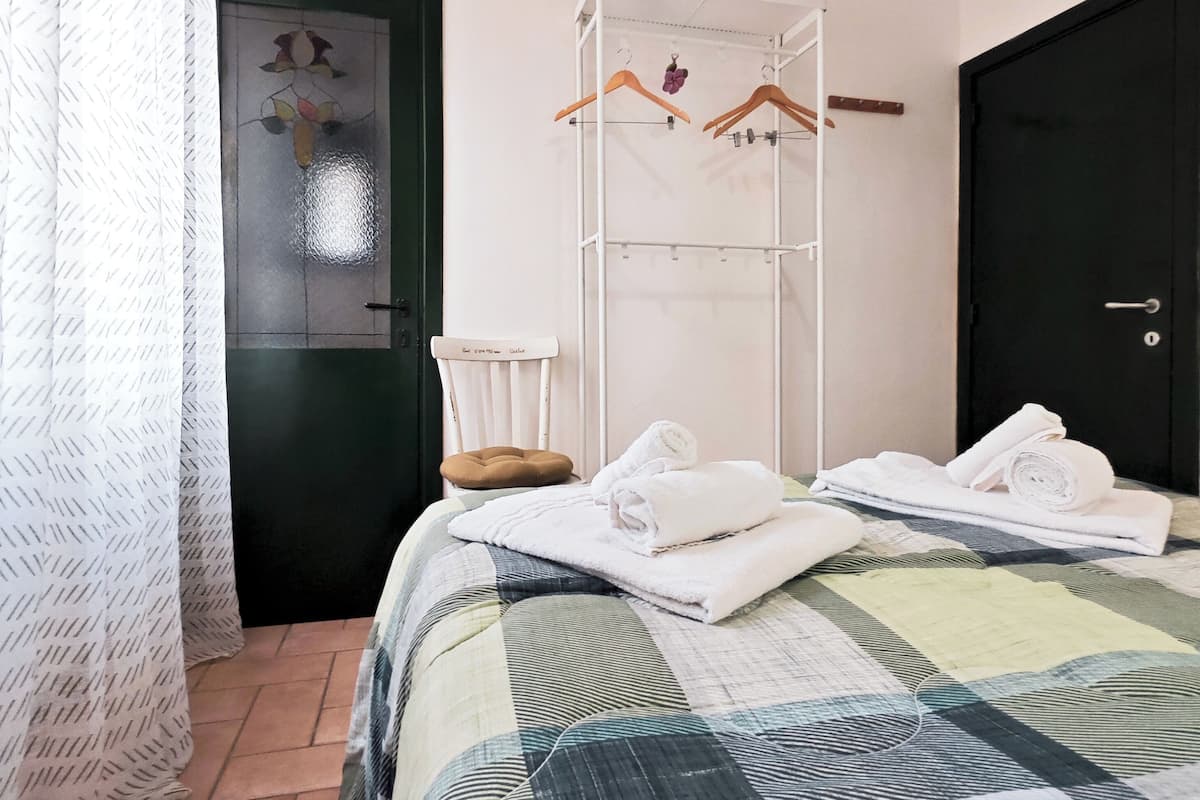 Quarto de hotel com uma cama, um porta-toalhas branco, uma porta preta e uma janela com cortina.