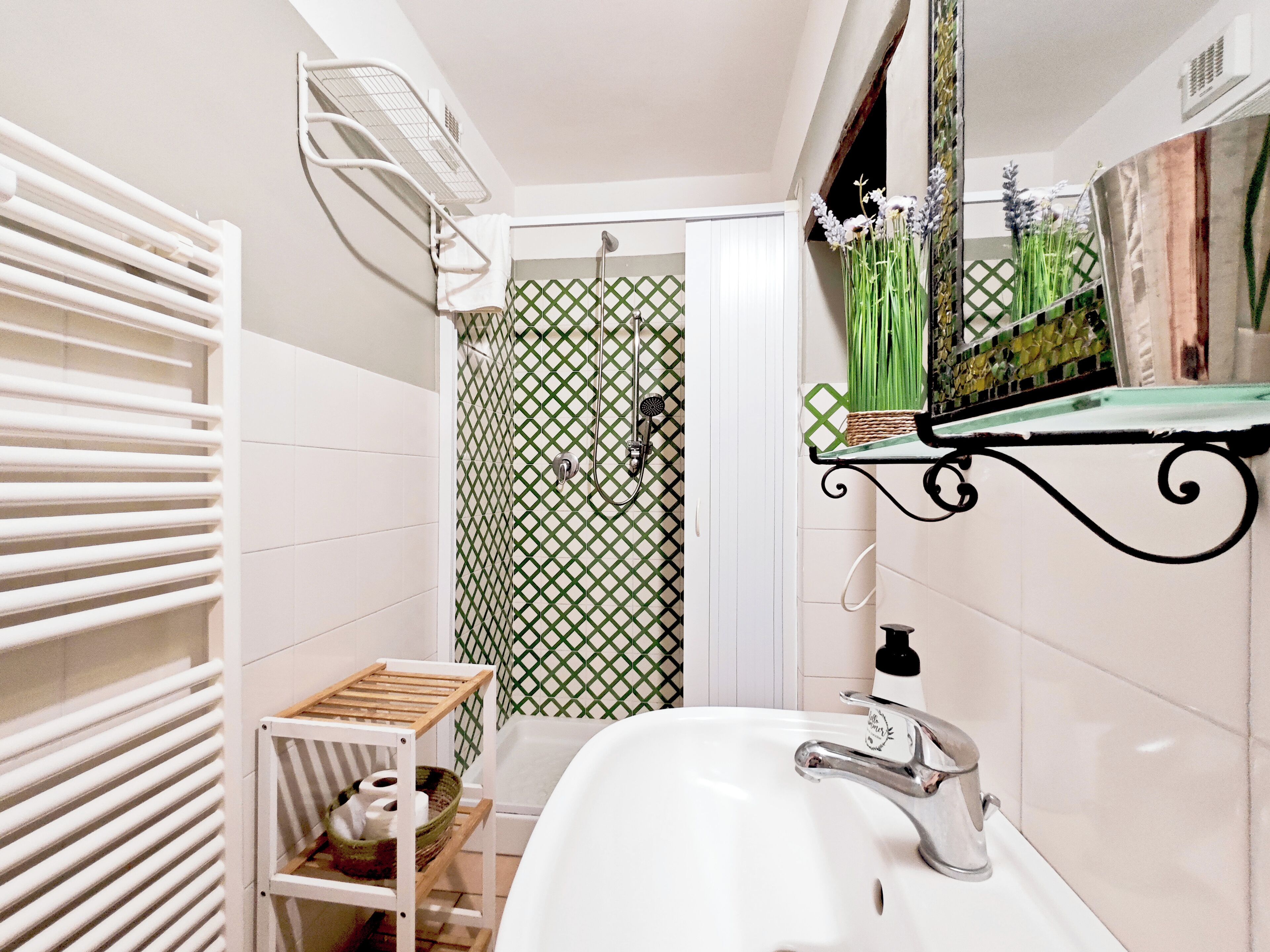 Un baño con un lavabo blanco, una ducha con puerta de diseño blanco y verde, y un toallero blanco.
