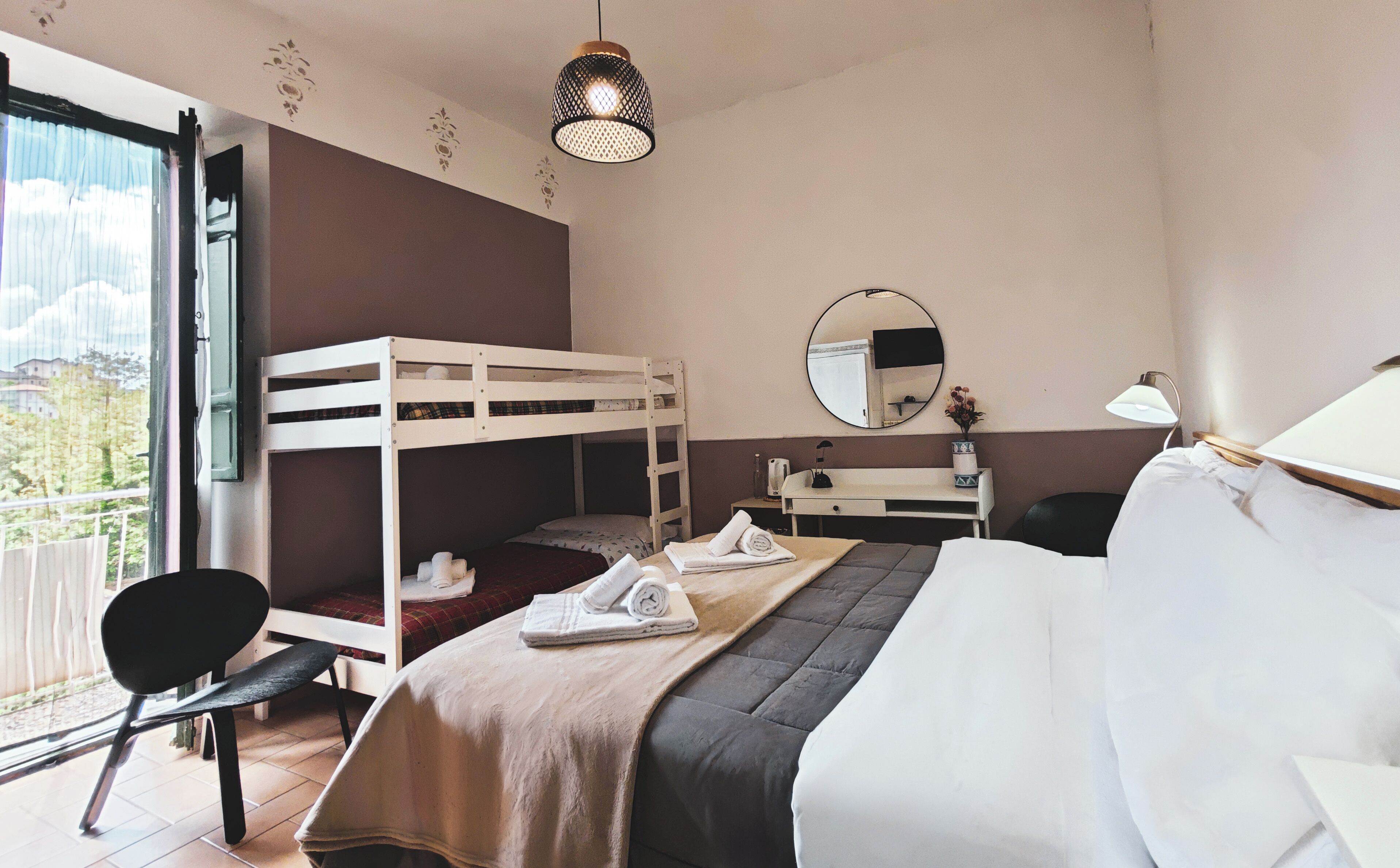 Ett hotellrum med en våningssäng, ett skrivbord med en spegel, en stol och en säng med en stor kudde.