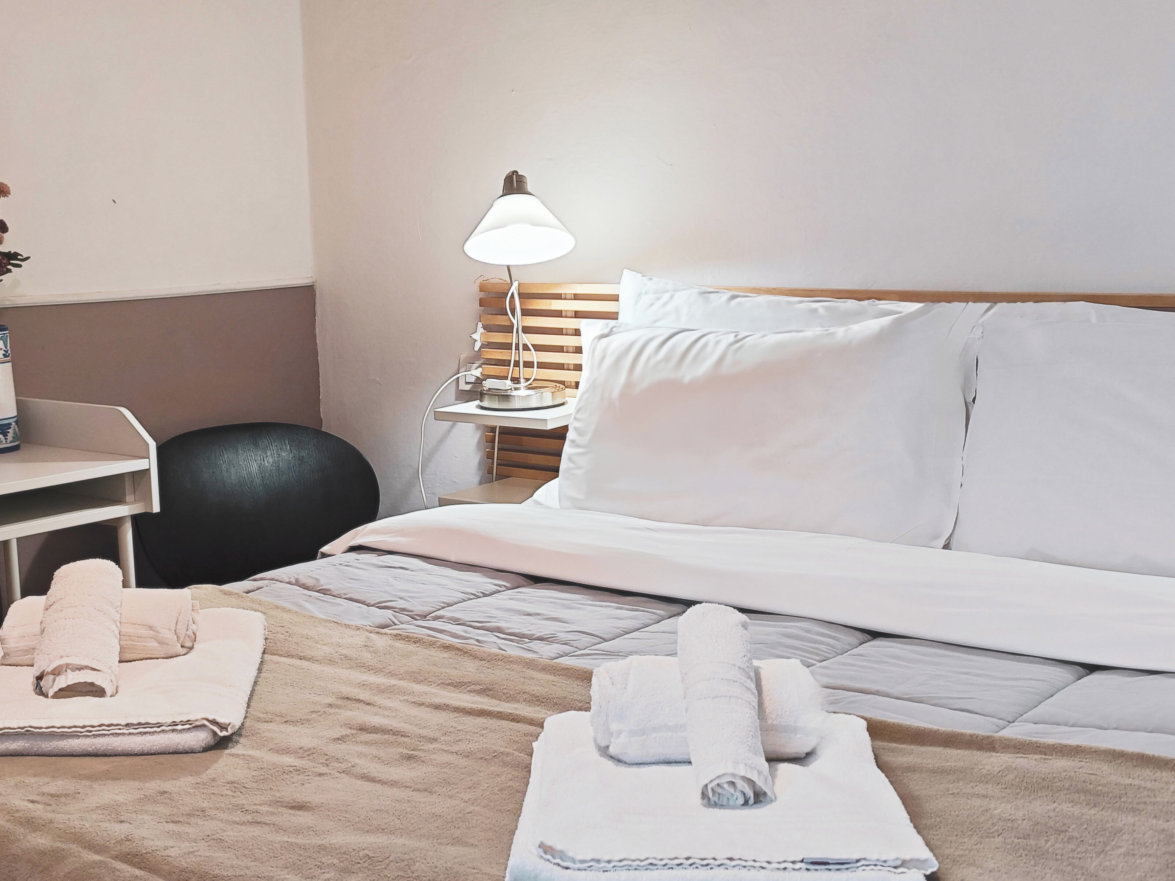 Ein Hotelzimmer mit Bett, Schreibtisch, Stuhl, Lampe und Handtüchern.