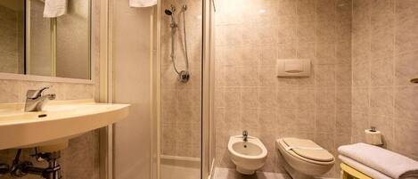 A bathroom with a glass-enclosed shower, a sink, a bidet, and a toilet.