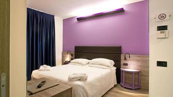 Una habitación de hotel moderna con cama, lámparas de noche, una mesita de noche y una pequeña mesa con un control remoto.