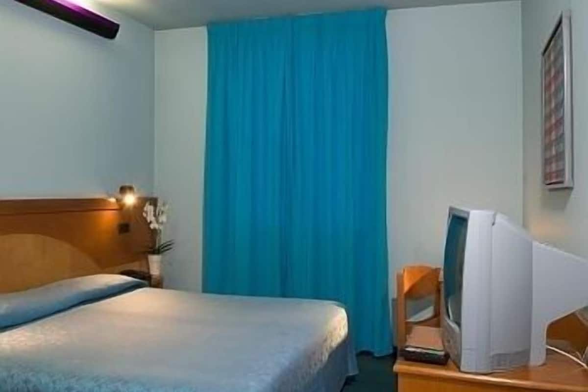 A hotel room with a bed, a desk with a television, and a window with curtains.
