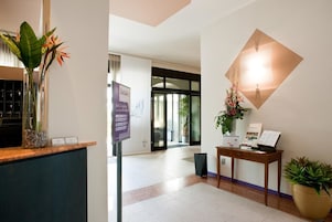 A reception area with a wooden counter, a glass vase with flowers, a wall-mounted light fixture, and a signboard.