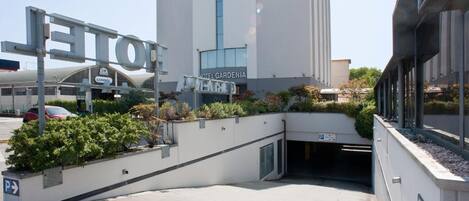 Una entrada de hotel moderna con un cartel que dice 'HOTEL GARDENIA' y un área de estacionamiento.