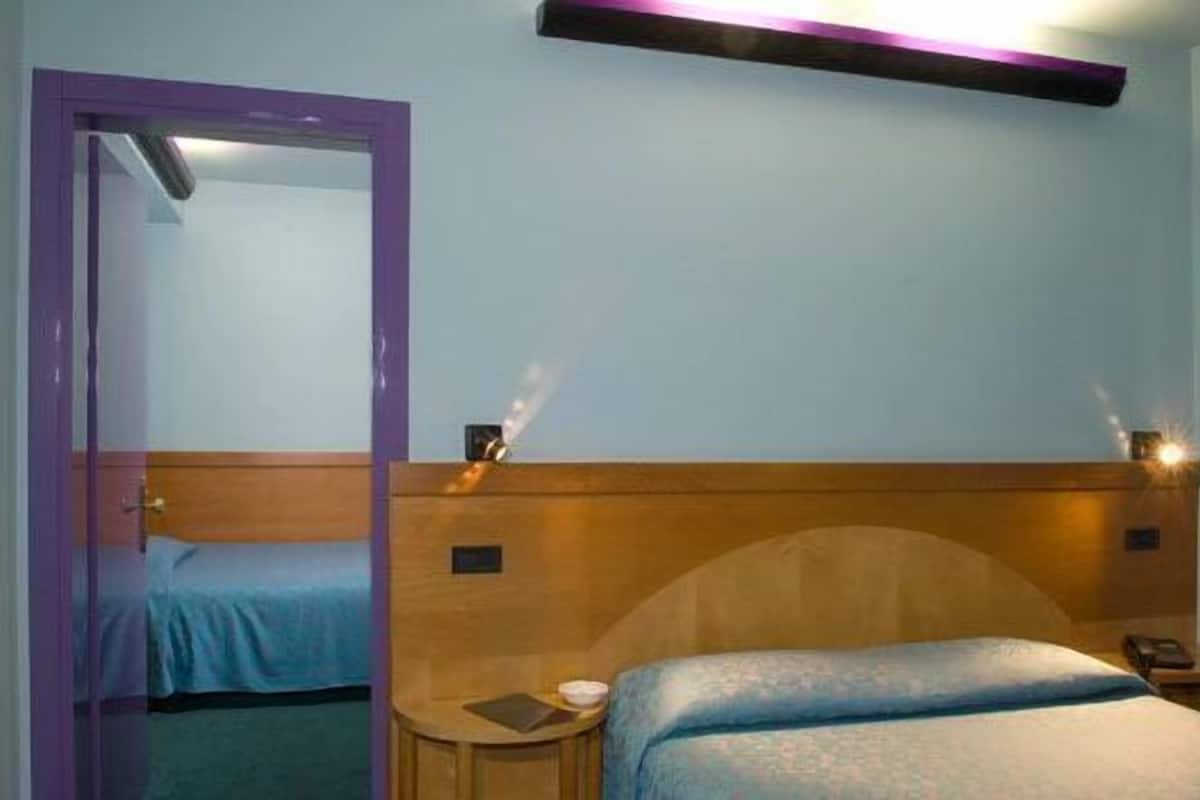 A hotel room with a wooden headboard, a bed with a blue bedspread, a bedside table with a lamp, and a mirror on the wall.